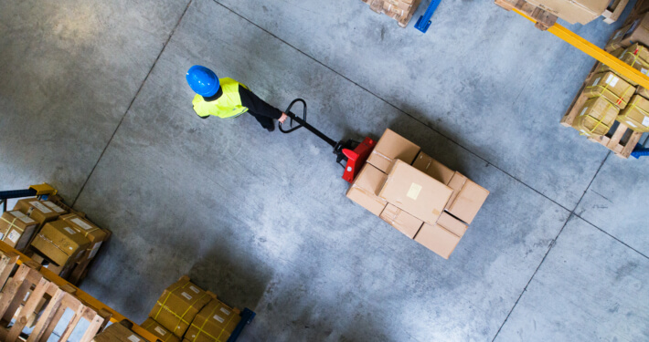 Sicht von oben auf einen Mitarbeiter in einem Logistikzentrum, der einen Wagen mit Paketen zieht.