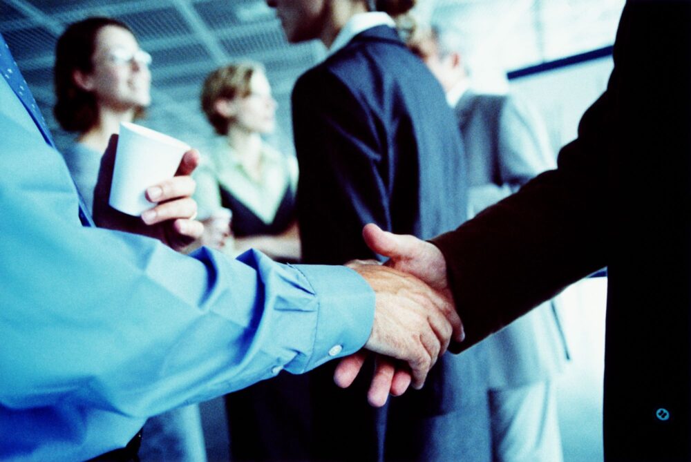 Zwei Geschäftsleute geben sich bei einer Franchising Messe einen Handschlag.