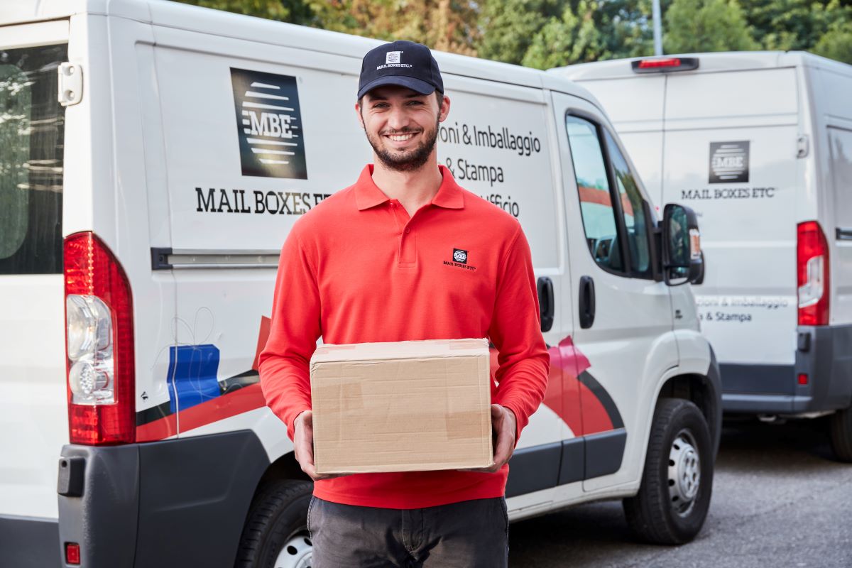 Mail Boxes Etc courier holding cardboard box, stood outside a van in Italy